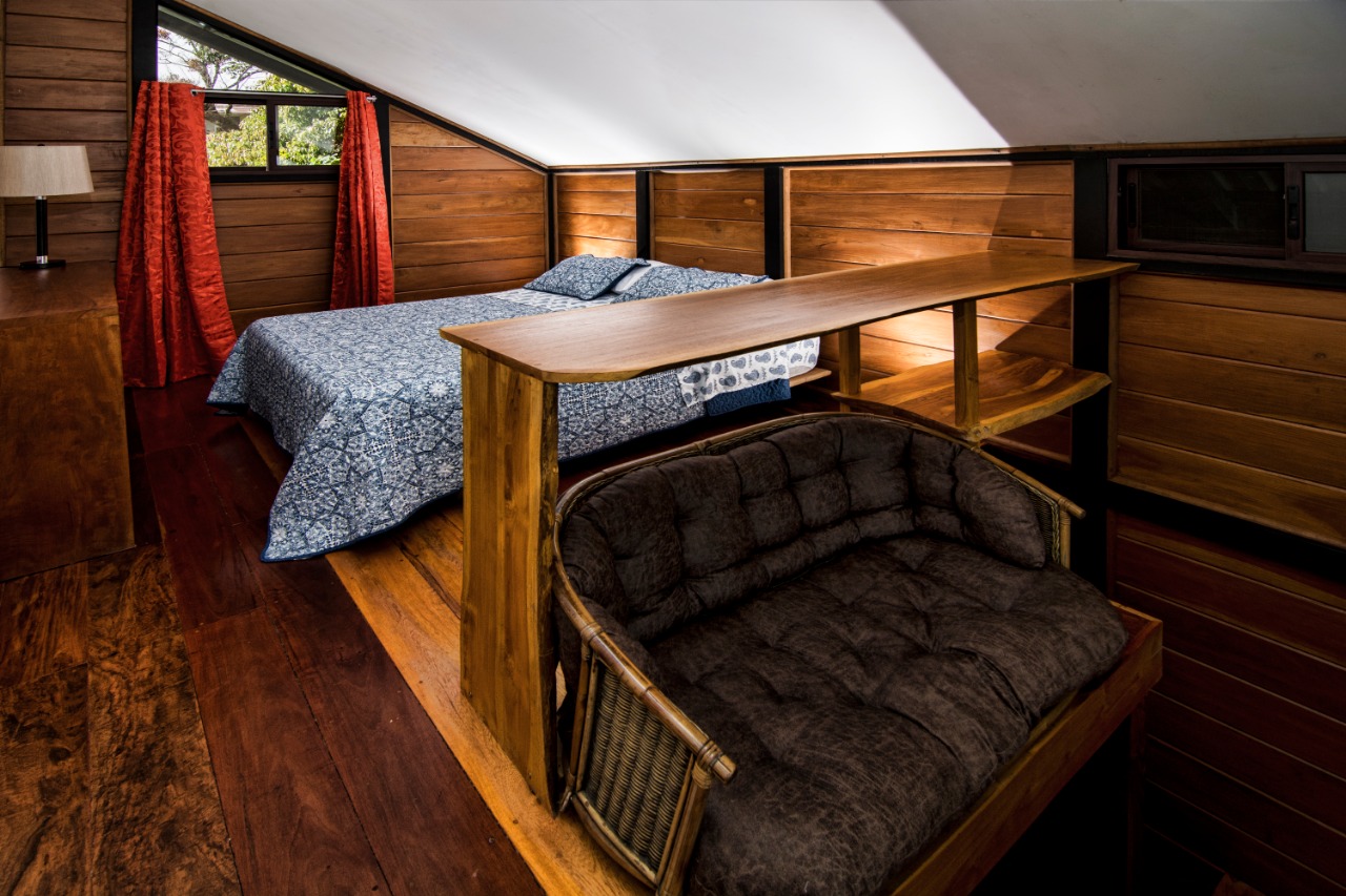 Segunda planta de la Guest House con cama queen y sofá bajo el techo inclinado