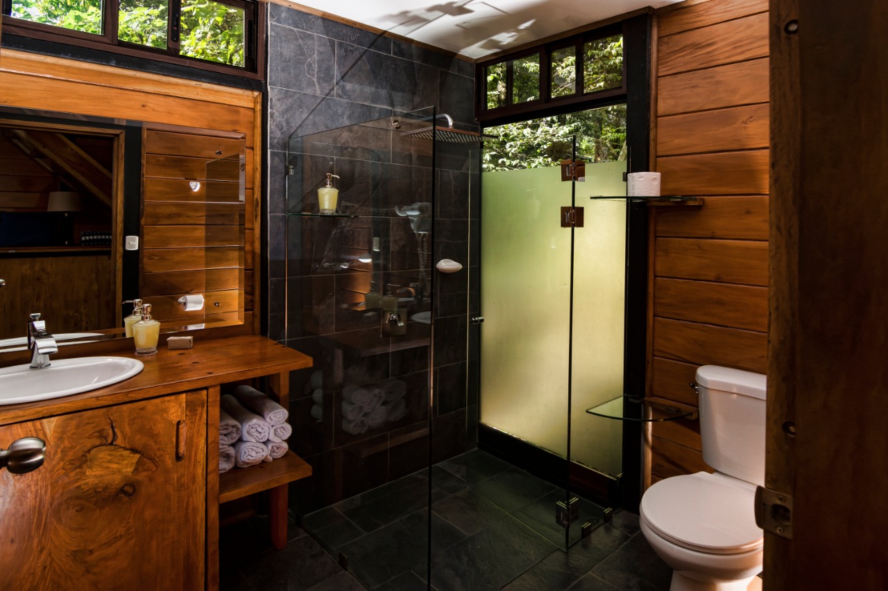 Baño de la Guest House con ducha de vidrio y acabados en madera y piedra