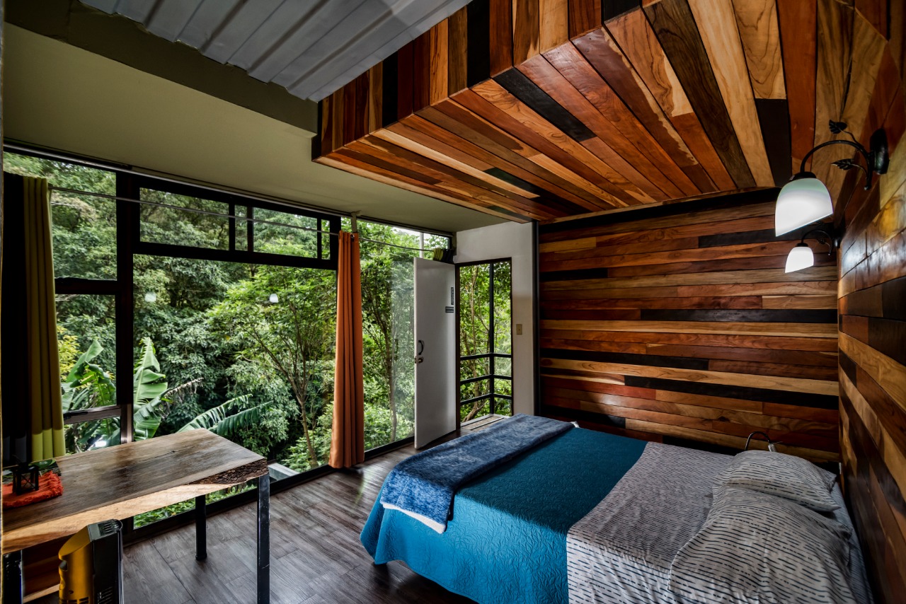 Dormitorio del Studio Maracuyá con cama queen, pared de maderas y ventanal al bosque nuboso